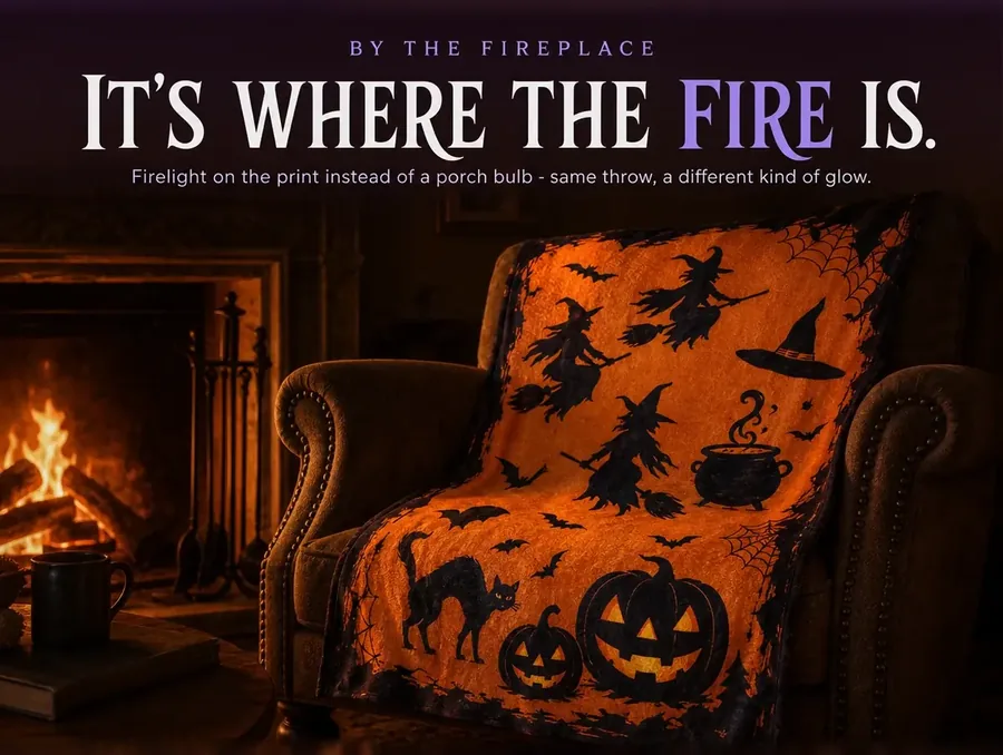 The witch-print throw over an armchair beside a lit fireplace, firelight flickering across the fabric.