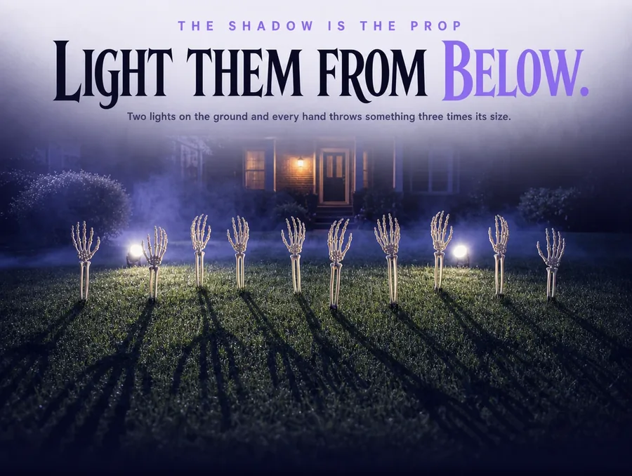 Arm stakes lit from below by two ground spotlights, long hand shadows stretching across the grass.