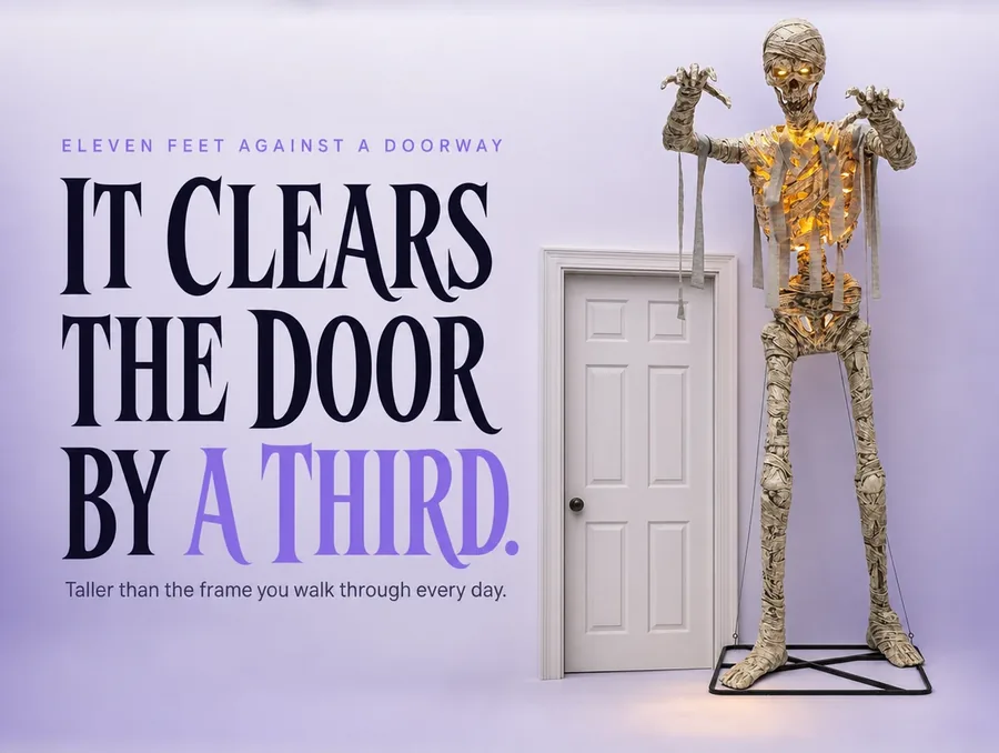 The mummy standing beside a plain front door, its head reaching well above the door frame.